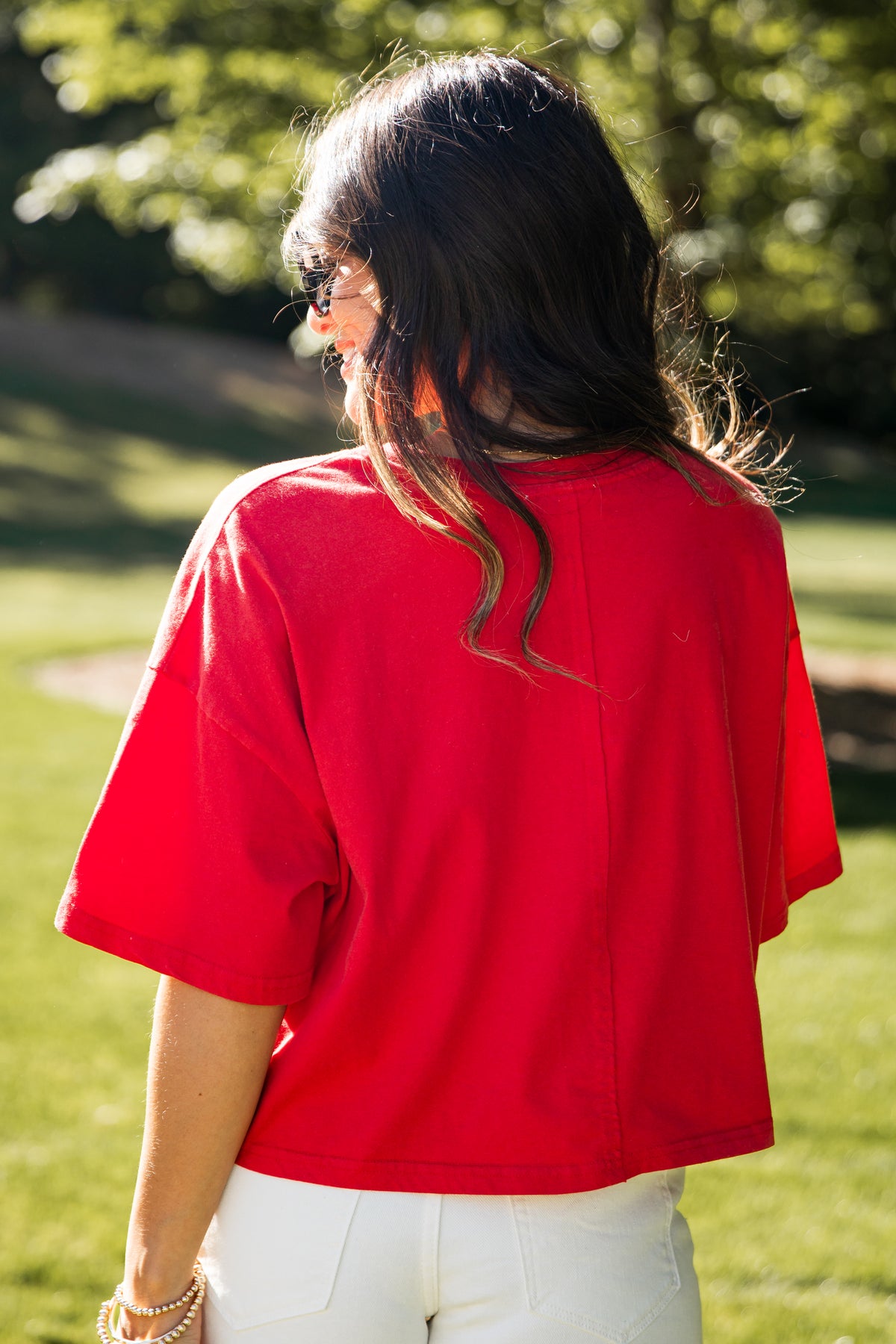 Person wearing a red shirt and white pants standing in a grassy area with trees in the background