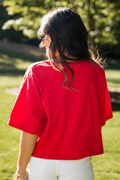 Person wearing a red shirt and white pants standing in a grassy area with trees in the background