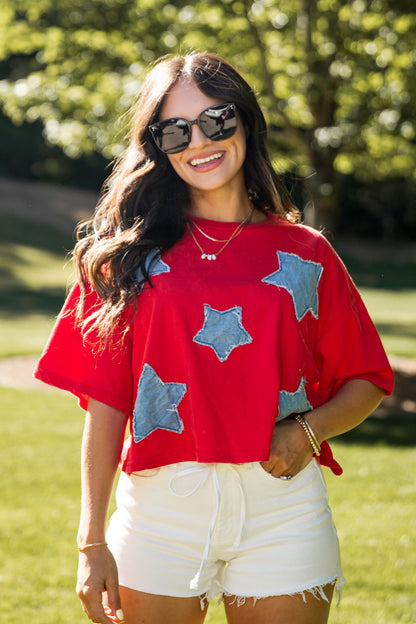 Woman wearing a red shirt with blue star patterns and white shorts outdoors.