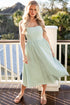 Woman in a light green dress standing on a balcony with trees in the background