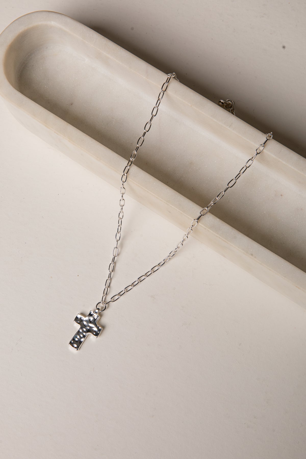 Silver necklace with a cross pendant on a beige surface