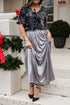 Woman wearing a black sequin top and silver skirt standing in front of a decorated fireplace.