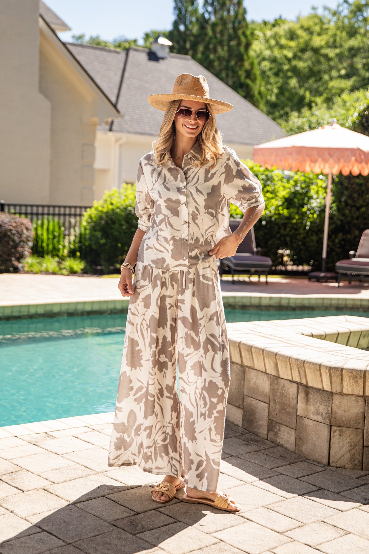 Woman in a floral fit and hat standing by a poolside.