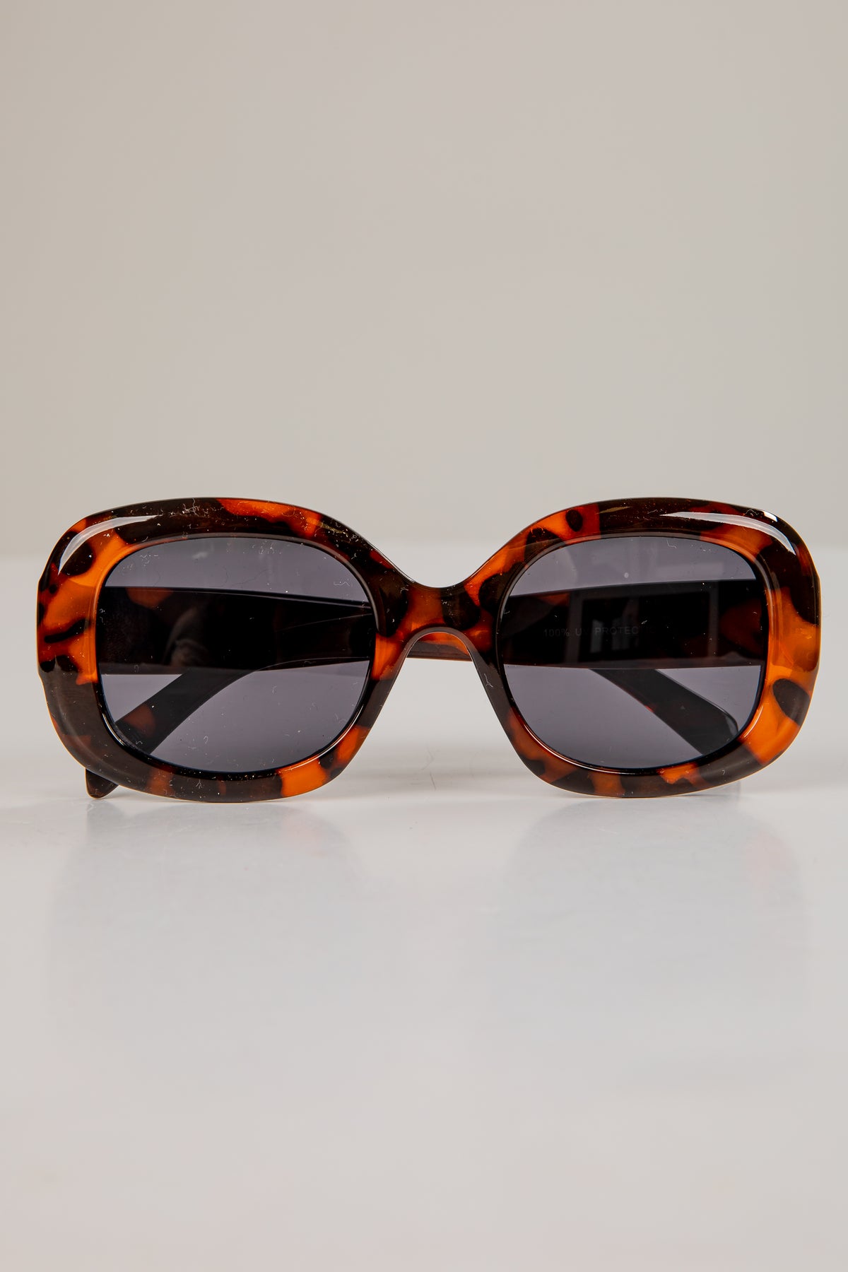 Sunglasses with tortoiseshell frame and dark lenses on a light gray background