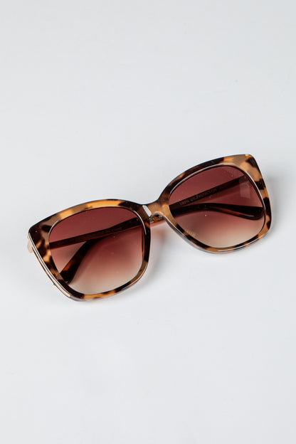 Sunglasses with tortoiseshell frame and brown gradient lenses on a light gray background