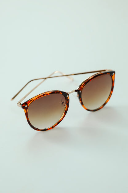 Sunglasses with tortoiseshell frame and gradient lenses on a light blue background