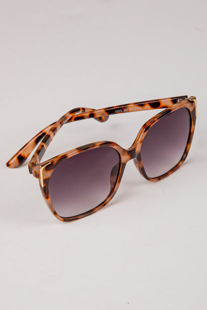 Sunglasses with tortoiseshell frame and dark lenses on a light gray background