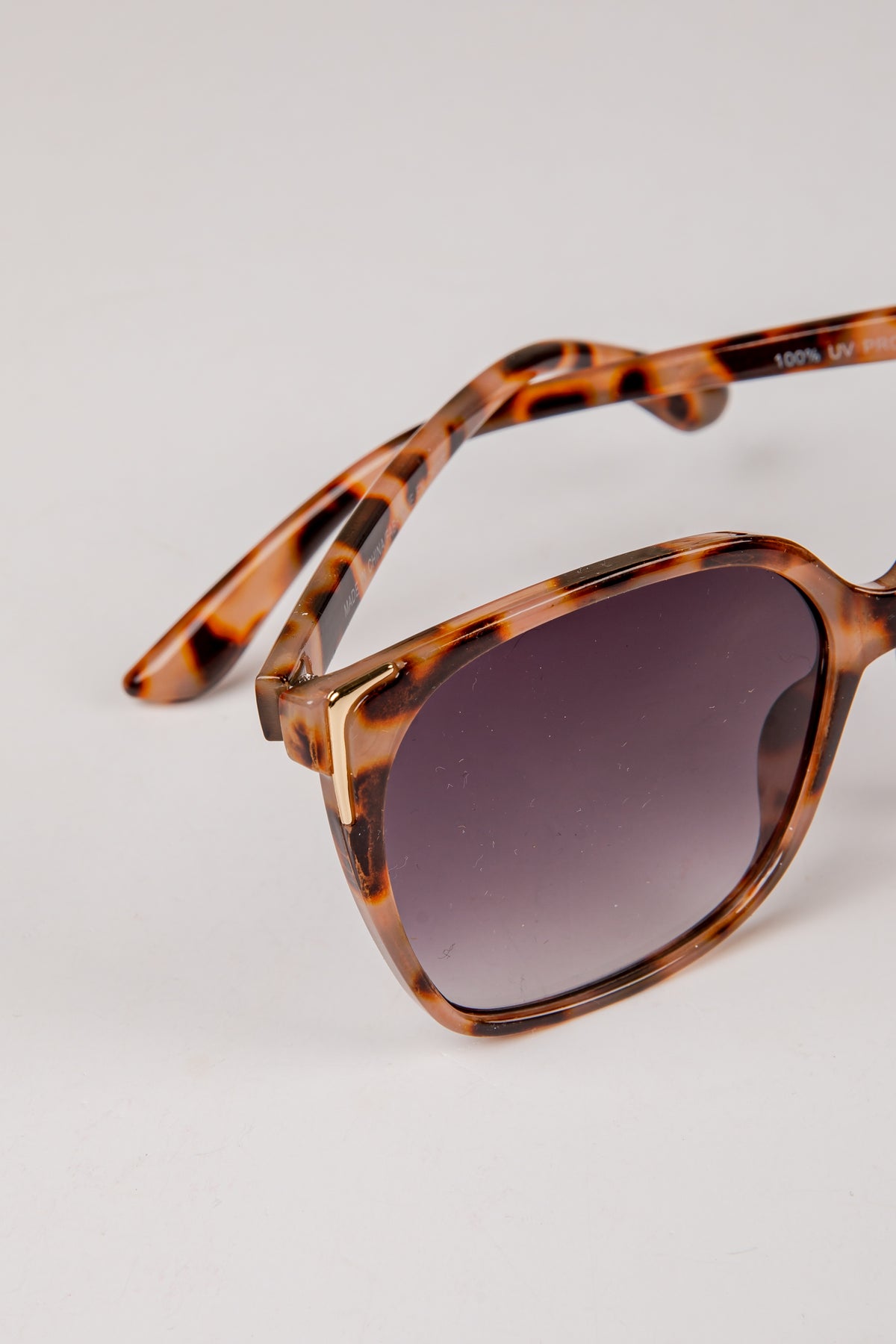 Sunglasses with tortoiseshell frame and dark lenses on a light gray background