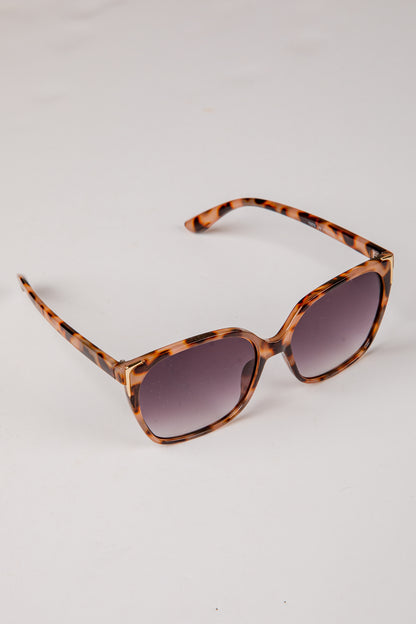 Sunglasses with tortoiseshell frame and dark lenses on a light gray background