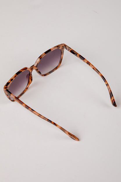 Sunglasses with tortoiseshell frame and dark lenses on a light gray background