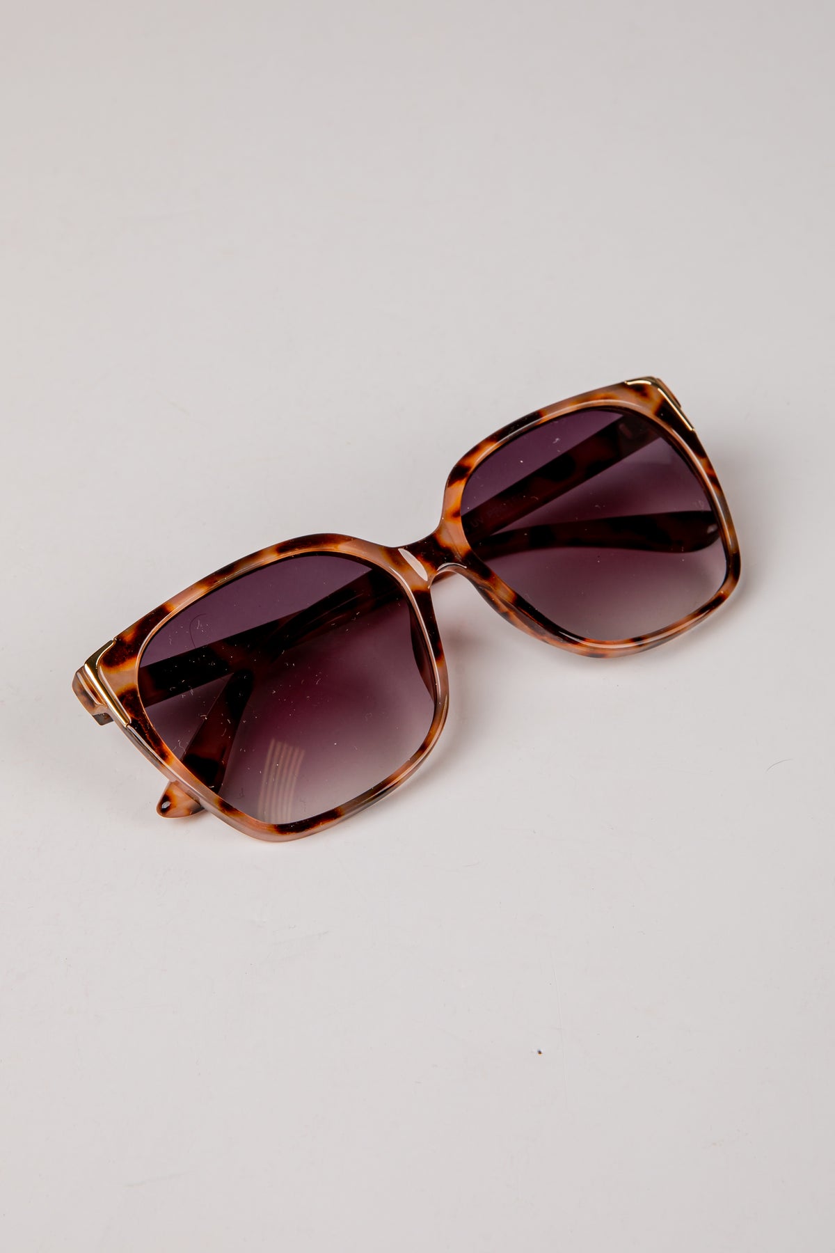Sunglasses with tortoiseshell frame and dark lenses on a light gray background