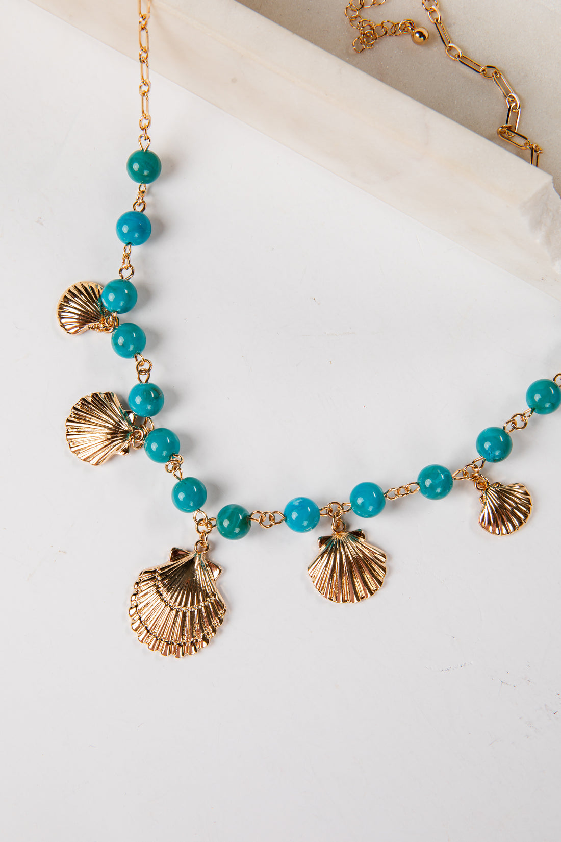 Necklace with turquoise beads and gold shell pendants on a white background