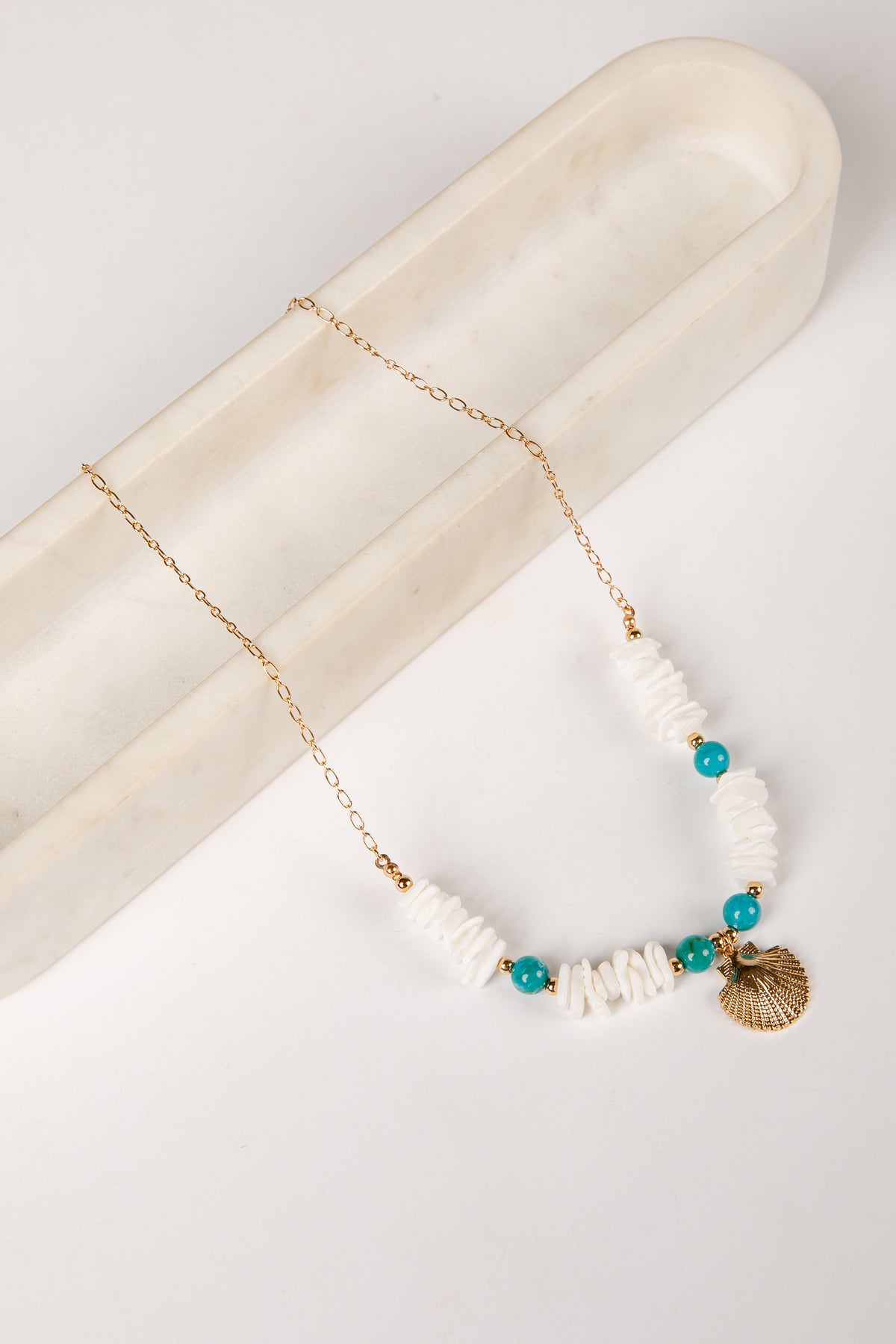 Necklace with white beads, turquoise stones, and a gold shell pendant on a marble surface.