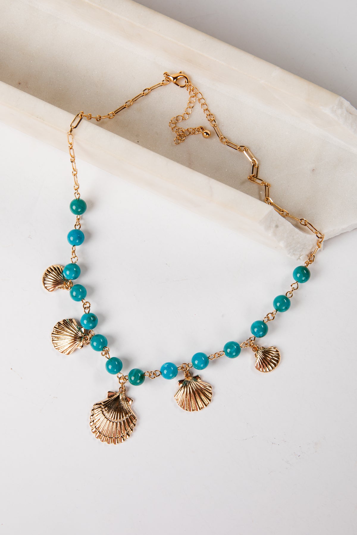 Necklace with turquoise beads and gold shell pendants on a marble surface