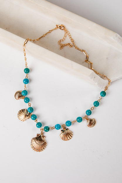 Necklace with turquoise beads and gold shell pendants on a marble surface