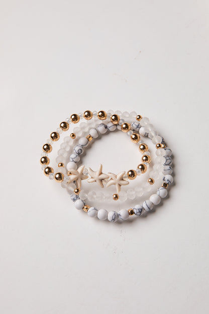 Set of three beaded bracelets with gold beads and starfish charm on a light background