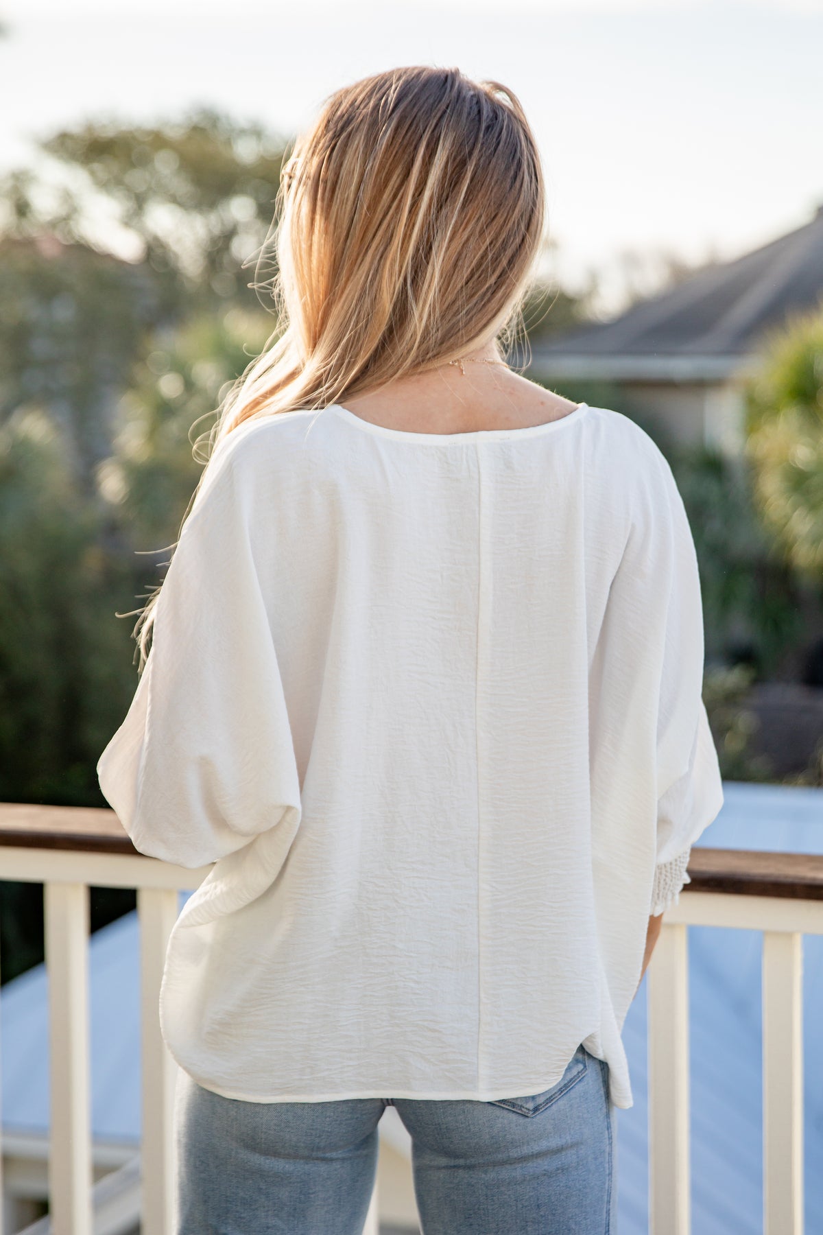 Person wearing a white blouse and jeans standing on a deck with blurred background