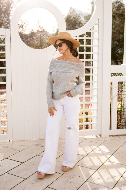 Woman wearing a gray sweater and white pants standing in front of a white lattice structure.