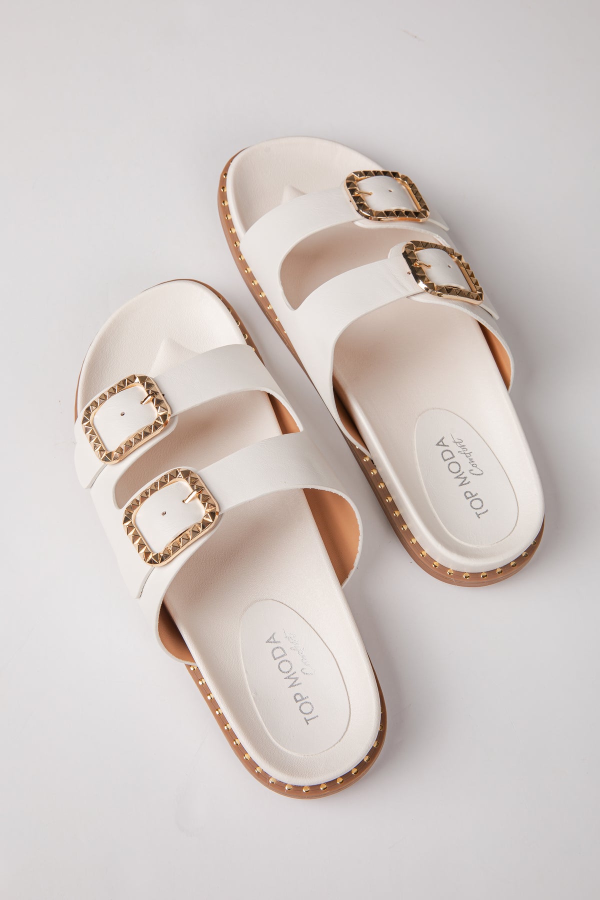 Pair of white sandals with gold buckles on a light gray background