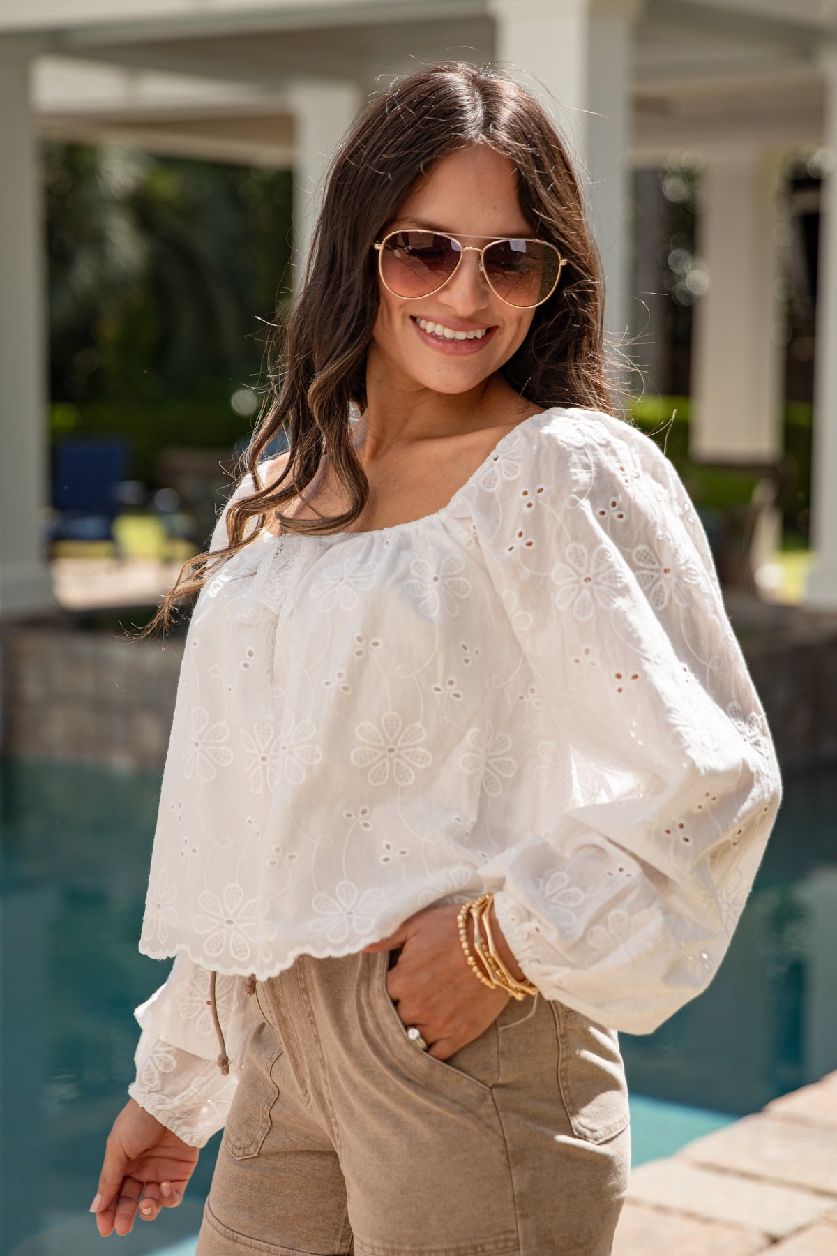 Woman wearing a white blouse and sunglasses by a poolside