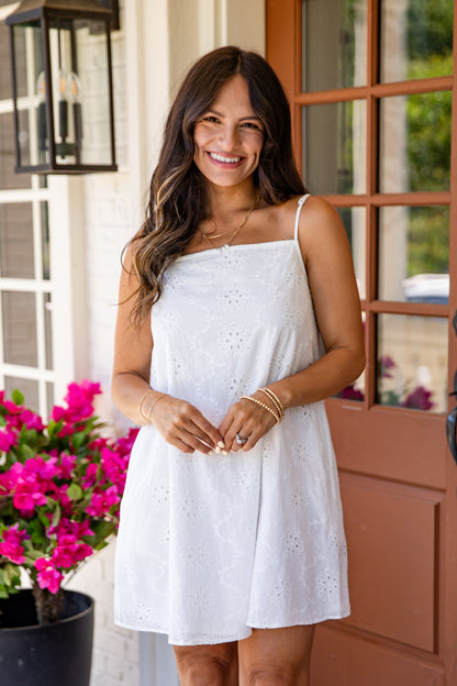Woman in a white dress standing outdoors with flowers and a door in the background