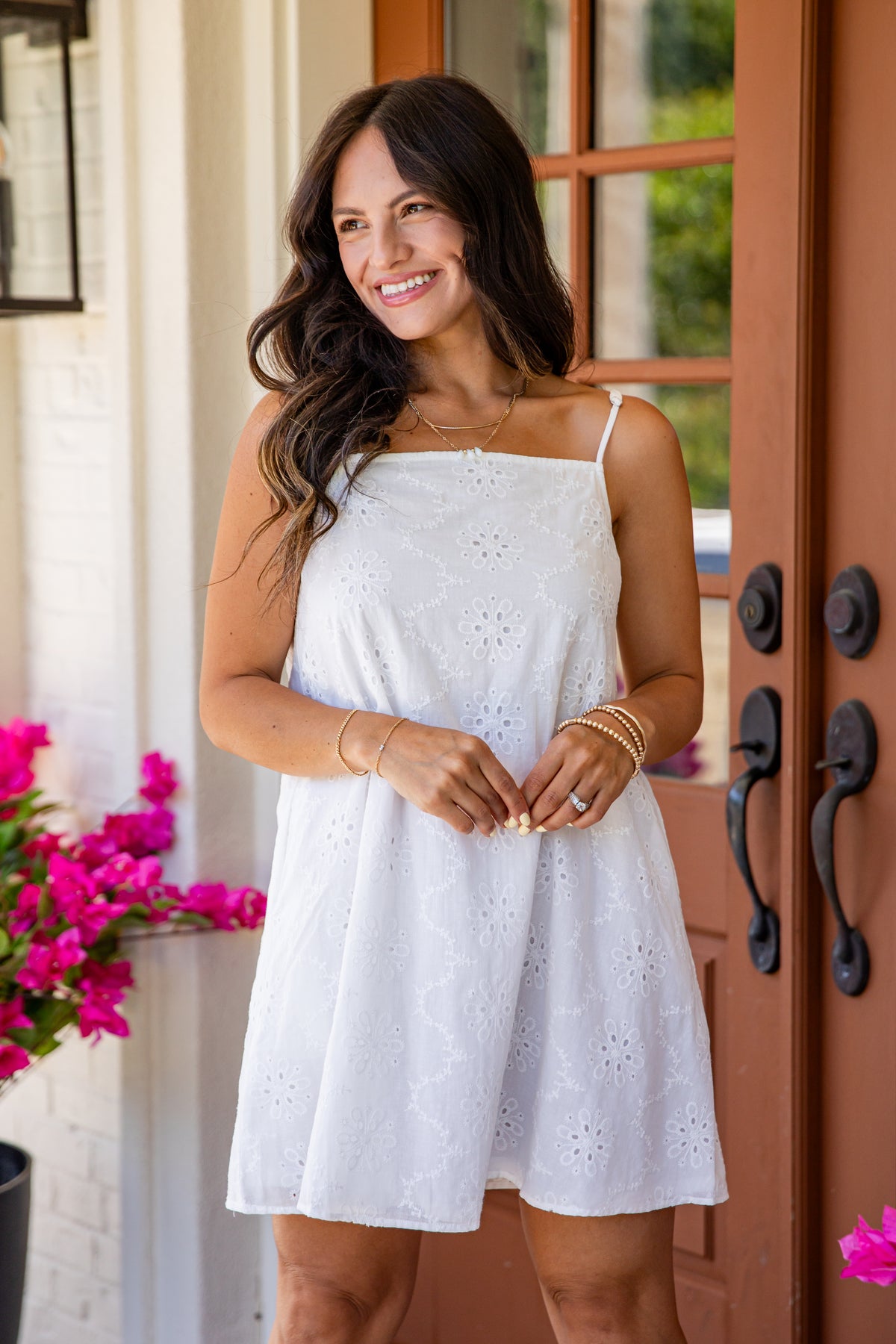 Woman in a white dress standing in front of a door with pink flowers.