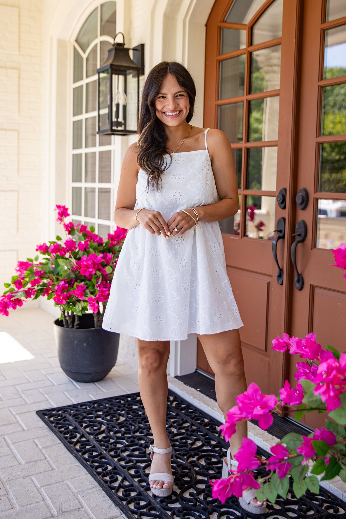 Woman in a white dress standing in front of a door with pink flowers.