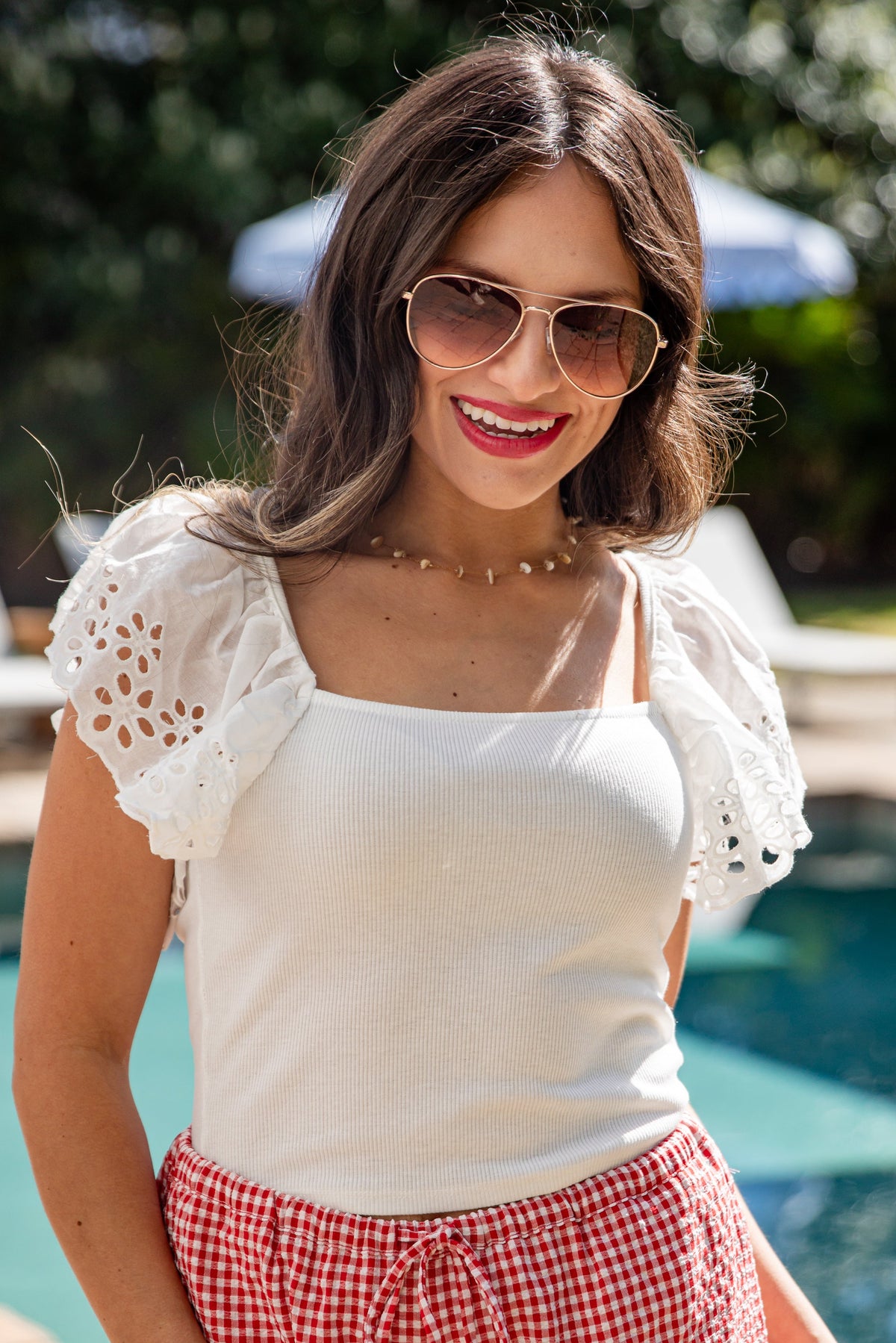 Woman in white top and red patterned shorts smiling poolside.