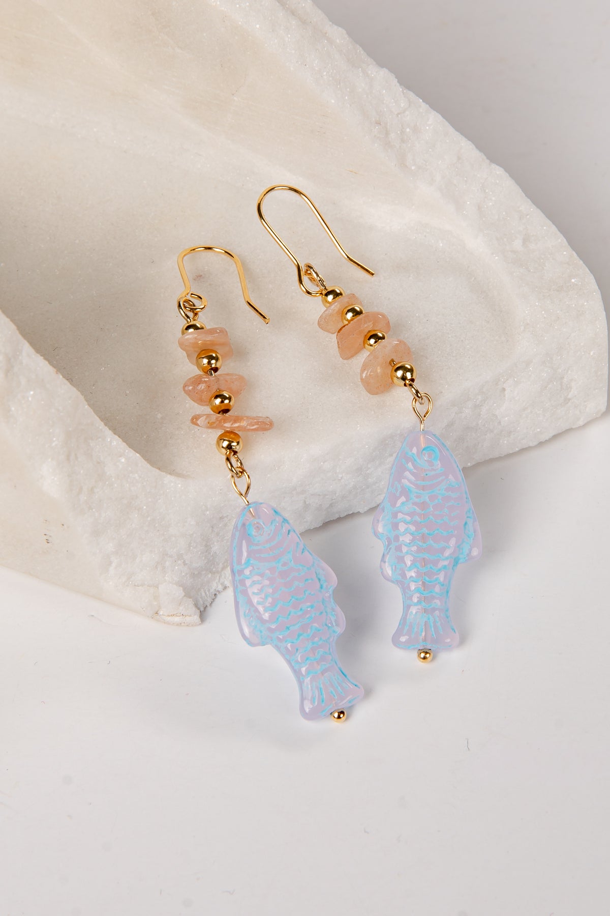 Earrings with blue fish-shaped beads and gold accents on a white shell background