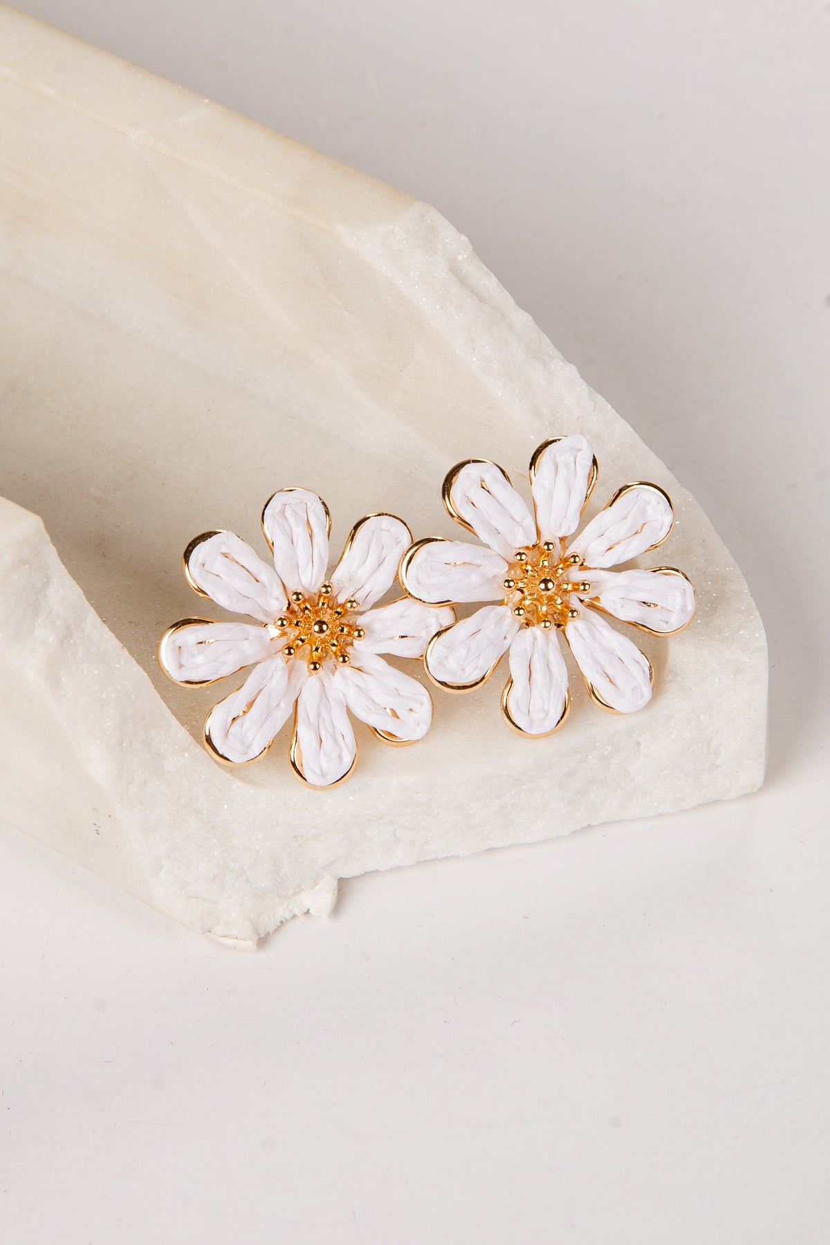 White daisy earrings with gold centers on a beige fabric background