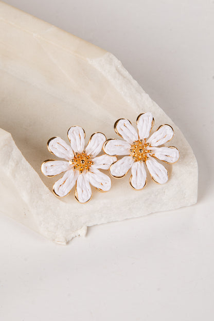 White daisy earrings with gold centers on a beige fabric background