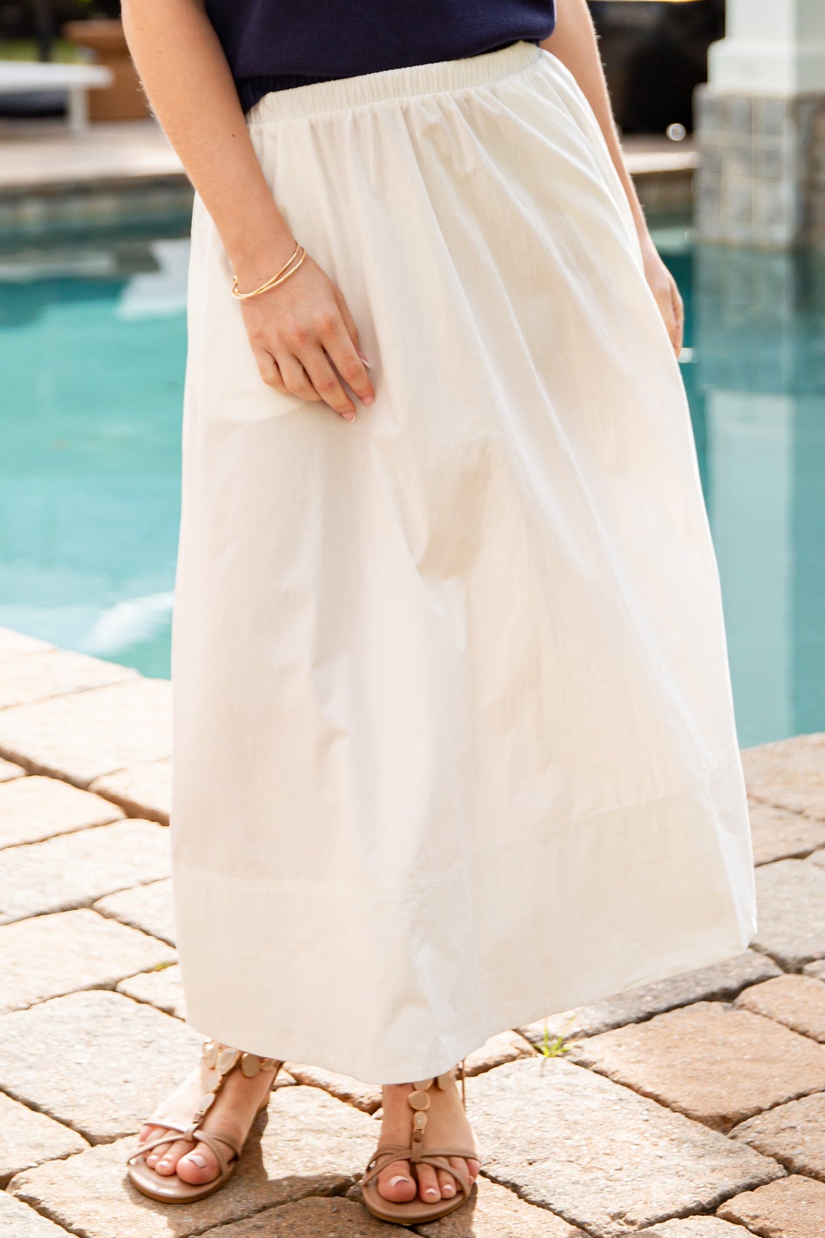 Person wearing a navy top and white skirt by a poolside