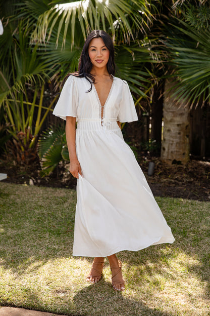 Woman in a white dress standing outdoors with greenery in the background