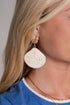 Close-up of a person wearing beige raffia earrings with a blue shirt and necklace.