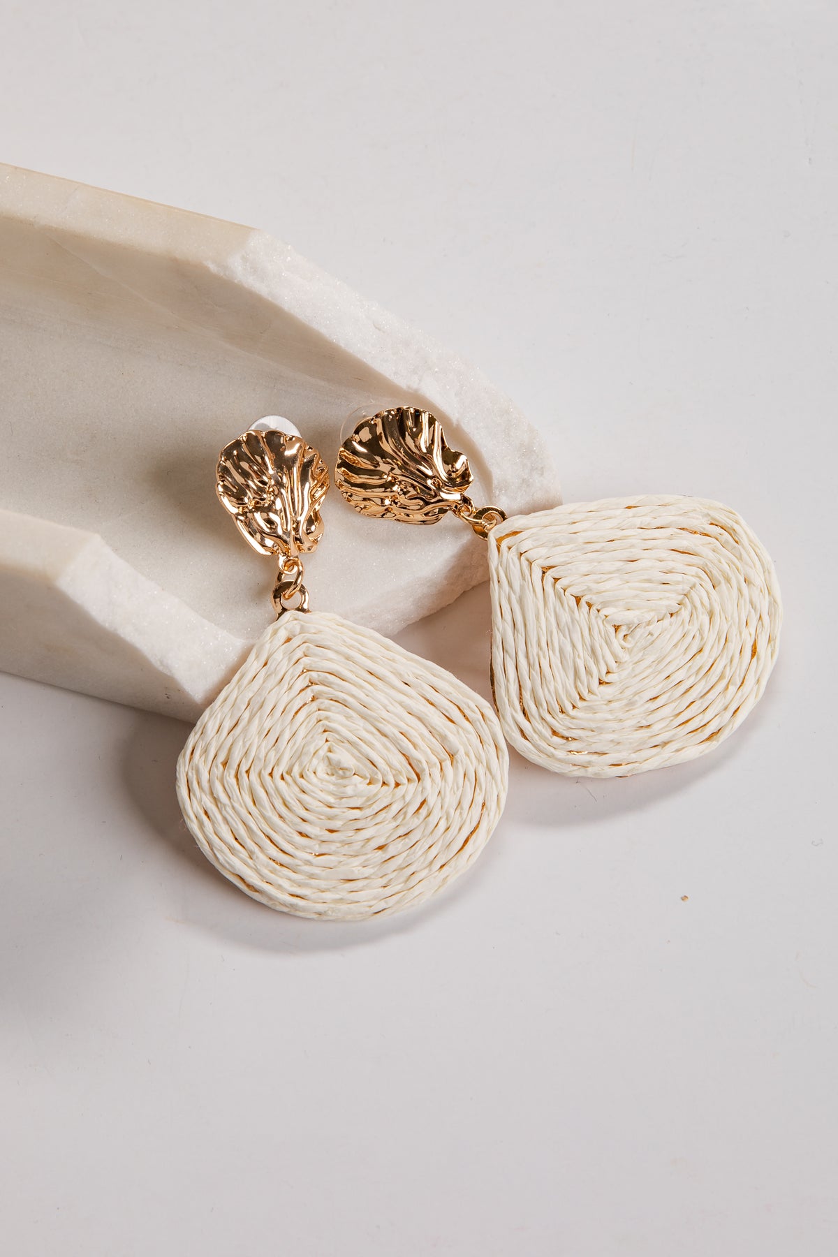 Pair of gold and cream earrings on a light background
