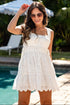 Woman in a white dress standing by a pool with sunglasses on