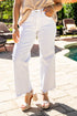 Person wearing white jeans and a beige top by a poolside with lounge chairs and an umbrella.