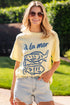 Woman wearing a yellow t-shirt with blue graphics and text, standing outdoors.