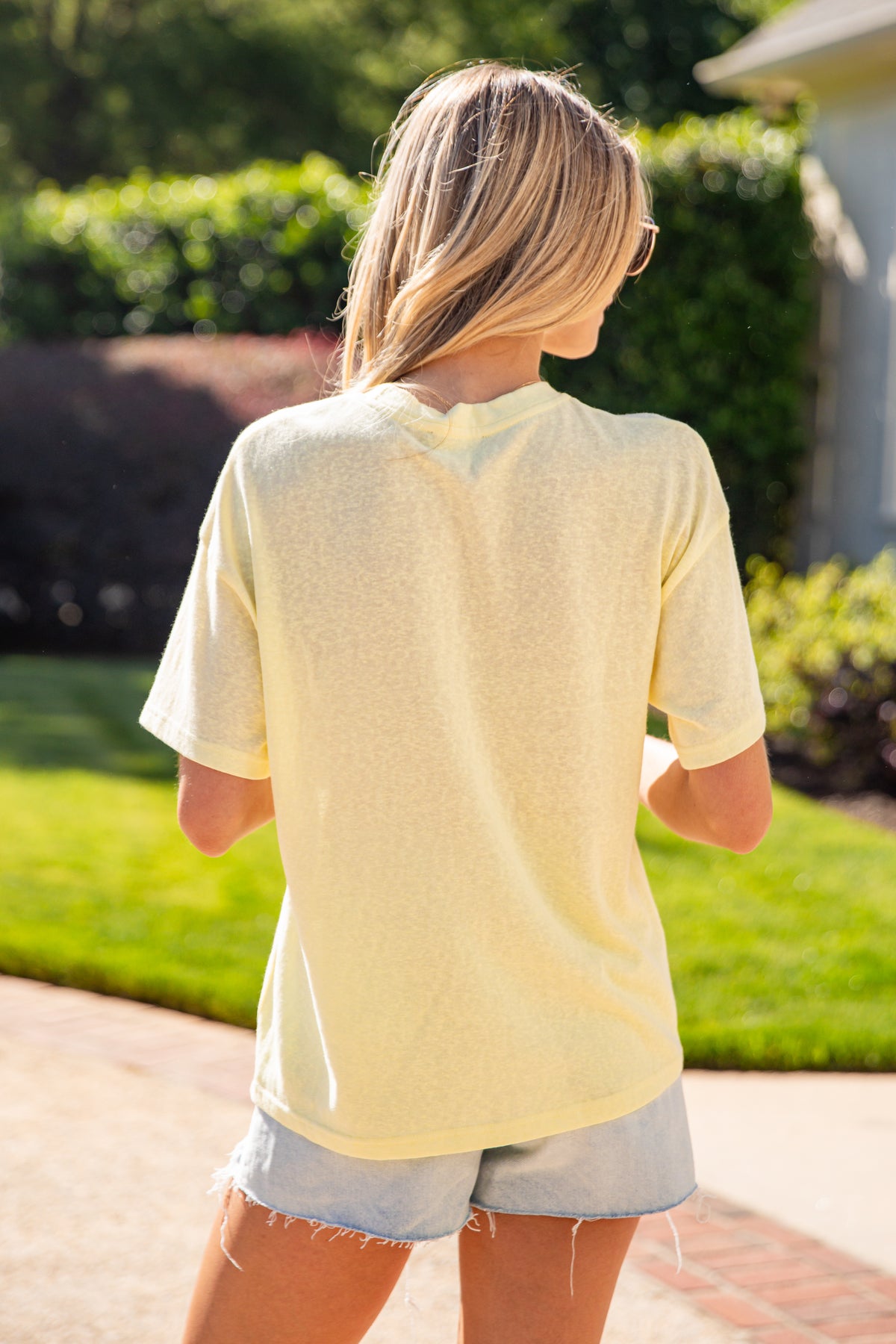 Person wearing a light yellow shirt and denim shorts standing outdoors.