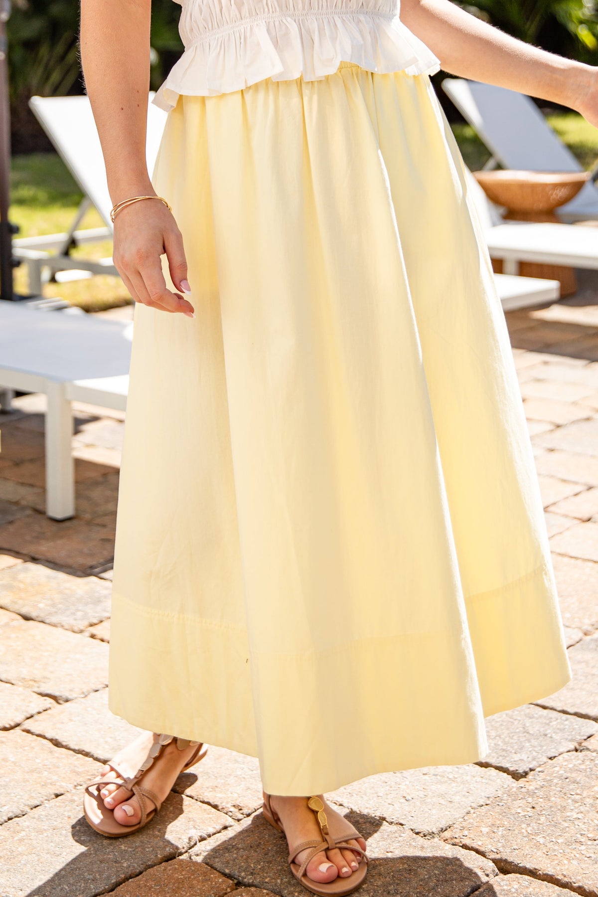 Person wearing a white top and yellow skirt standing on a patio.