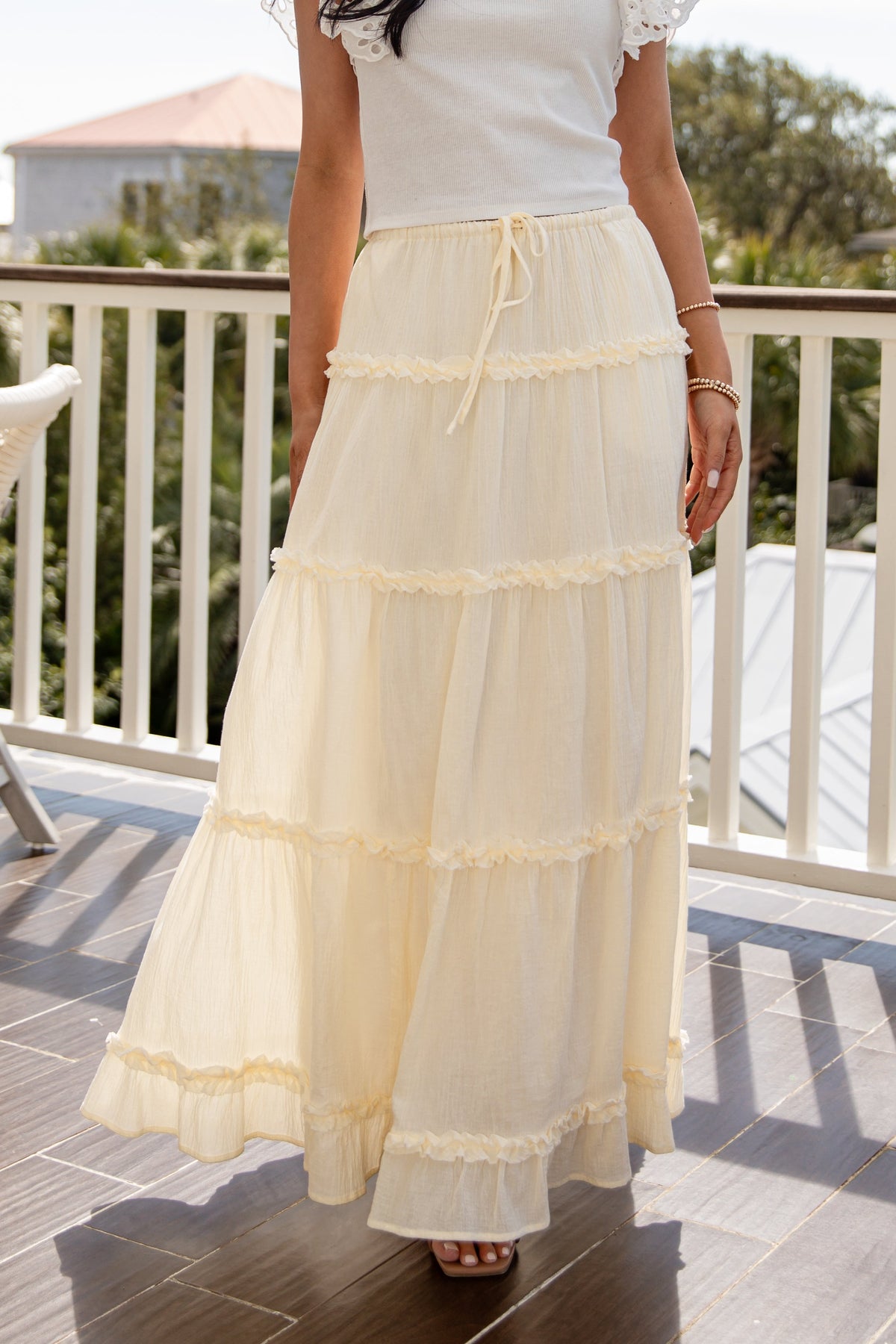 Person wearing a white lace top and cream-colored skirt on a balcony.