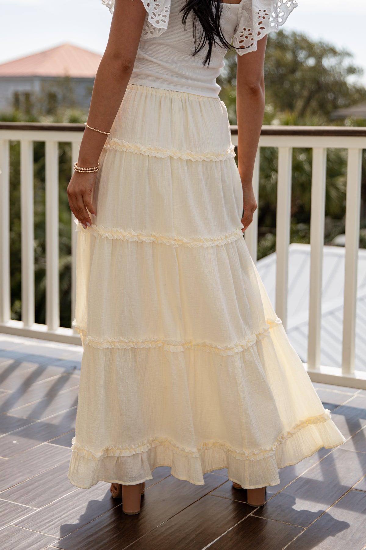 Person wearing a white lace top and cream-colored tiered skirt on a balcony.