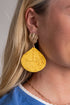 Close-up of a person wearing gold earrings with yellow teardrop-shaped pendants.