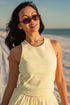 Woman in a yellow dress and sunglasses standing on a sandy beach.