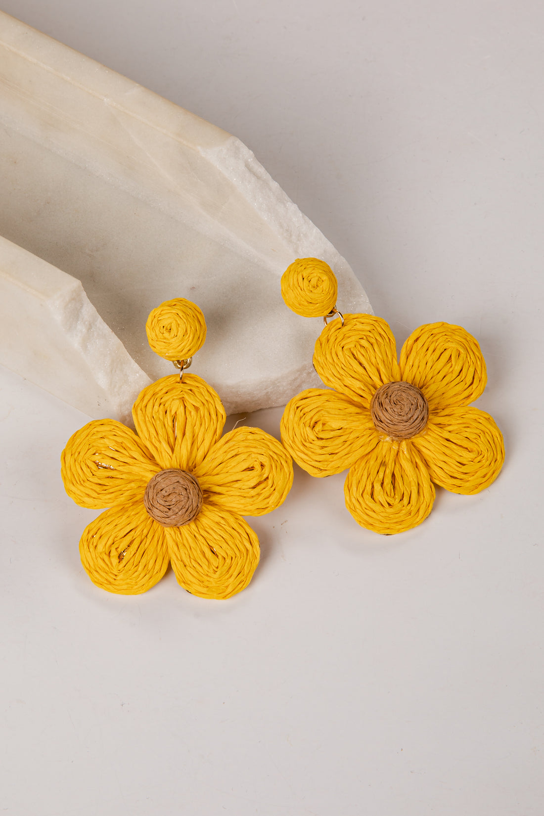 Yellow flower-shaped earrings on a marble surface